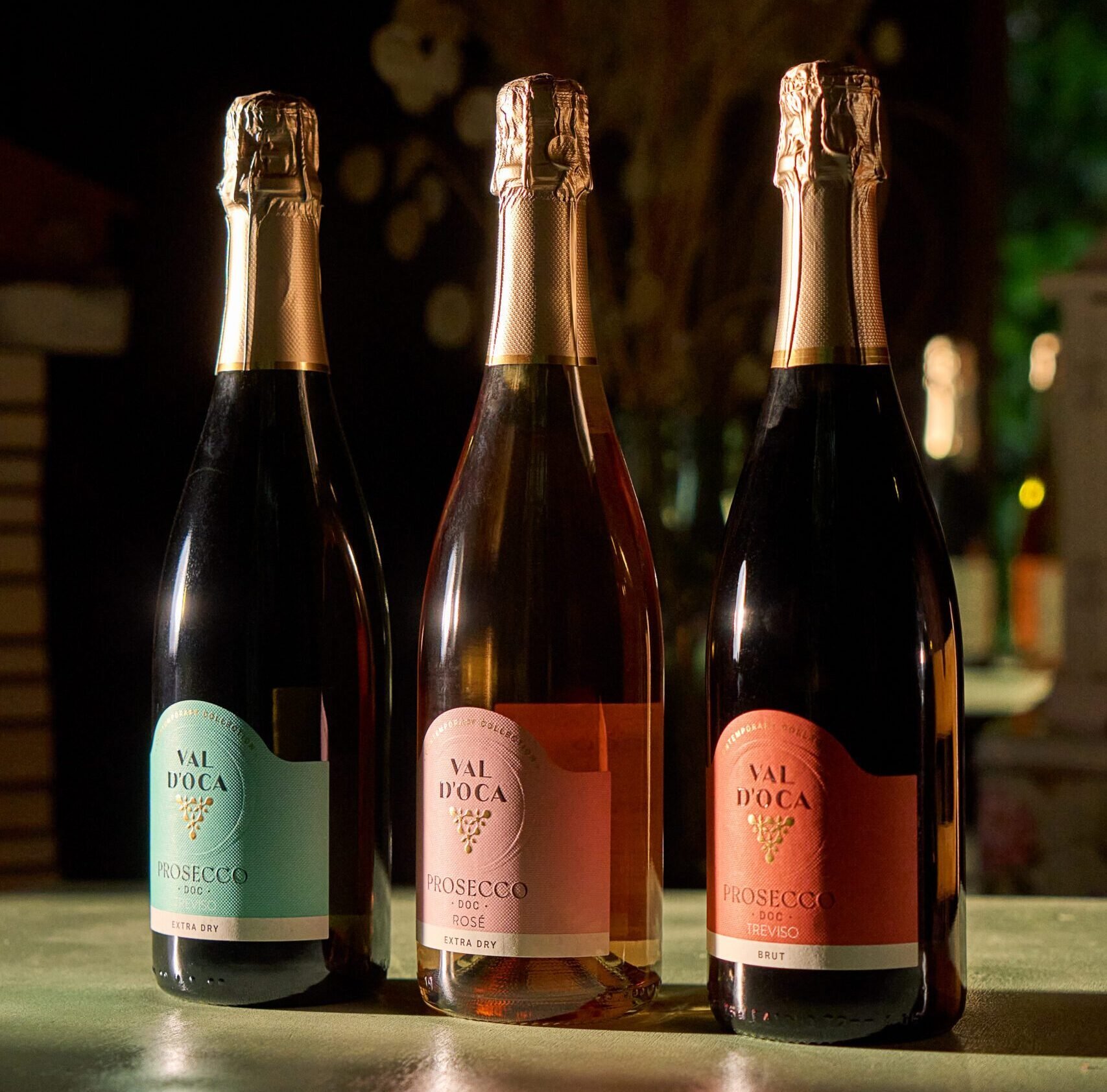 Tre bottiglie Val d'Oca Prosecco DOC con etichette verde Extra Dry, rosa Rosé e corallo Treviso Brut su un tavolo